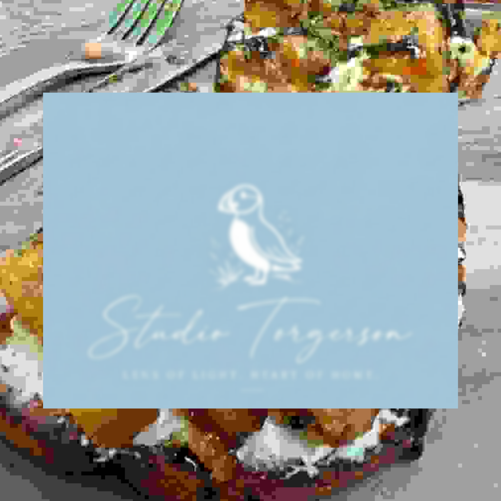 A square light blue card or label with a white puffin illustration and the text 'Studio Torgerson' over a blurred food background.